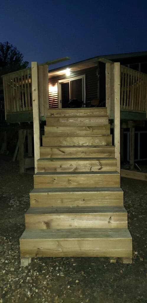 New wood stairs leading up to a deck with the porch light on